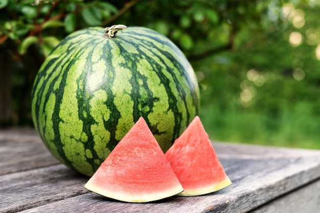 Melancia madura de baga de verão e fatias em uma mesa de madeira ao ar livre copie o espaço