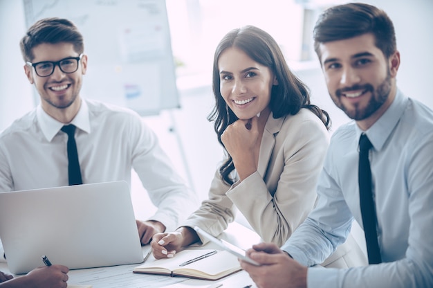 Melhor equipe de negócios. Grupo de colegas de trabalho alegres, olhando para a câmera com um sorriso, enquanto estão sentados à mesa do escritório