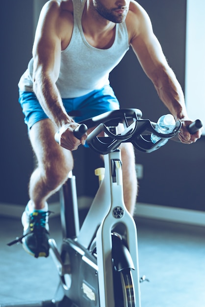 Foto melhor máquina interna para perda de peso. parte de um jovem em roupas esportivas, pedalando na academia