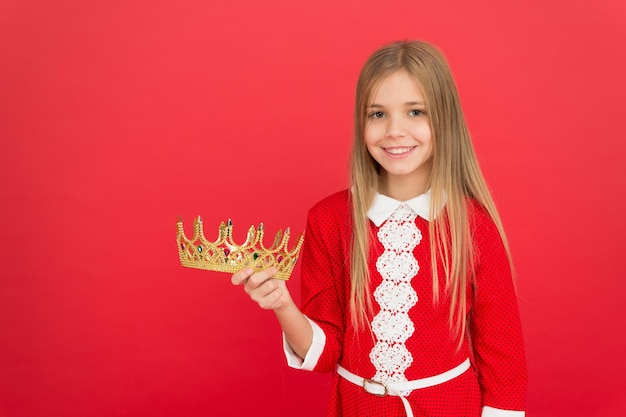 Melhor prêmio para mim. Criança segura o símbolo da coroa dourada da princesa. Conceito de infância feliz. Toda garota que sonha se torna princesa. Senhora pequena princesa. Sorriso fofo garota segurar a coroa enquanto fica o fundo vermelho.