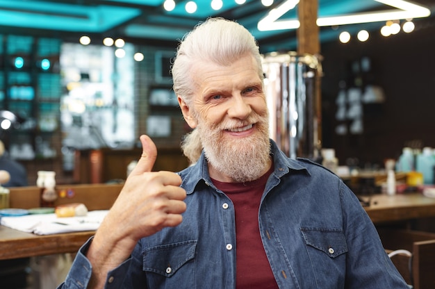 Melhor serviço. Homem barbudo encantado e positivo mantendo um sorriso no rosto enquanto mostra o polegar