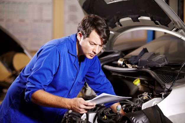 É melhor verificar a fiação Um mecânico masculino lendo alguns papéis enquanto trabalha no motor de um carro