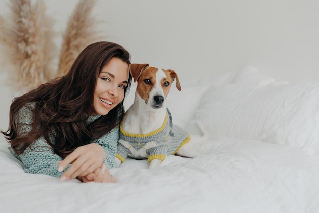 Melhores amigos A mulher atraente satisfeita fica perto do cão jack russell terrier expressa amor e cuidado com as brincadeiras favoritas do animal de estimação com animais domésticos relaxam juntos no cobertor branco Conceito de cuidados com animais