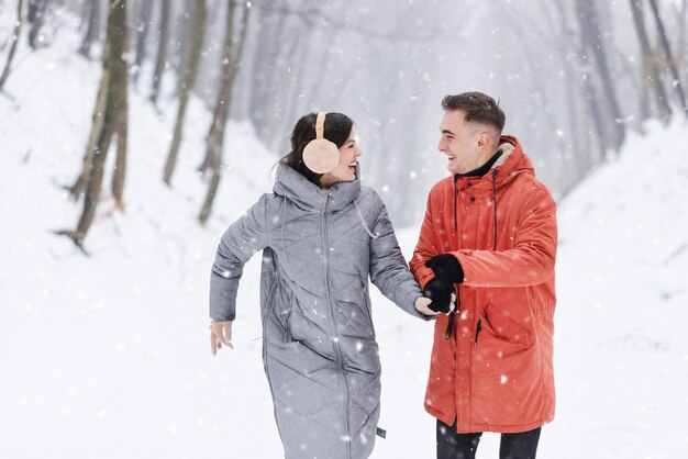 Melhores amigos com mochilas correndo de mãos dadas na floresta de neve de inverno