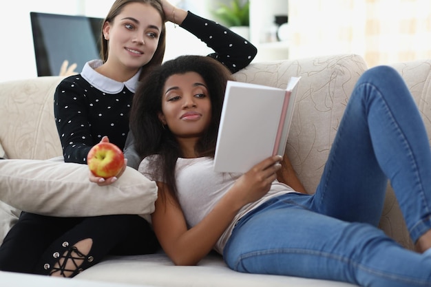 Melhores amigos lendo livro relaxando na maçã do sofá para uma atmosfera relaxante de lanche