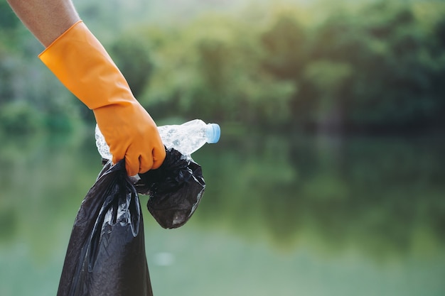 Foto melhoria do meio ambiente luvas laranja gentis, voluntários e ecologicamente corretos, segurando uma garrafa de água de plástico