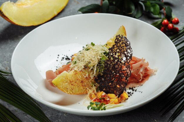 Melón al horno con queso parmesano y jamón en una placa blanca.