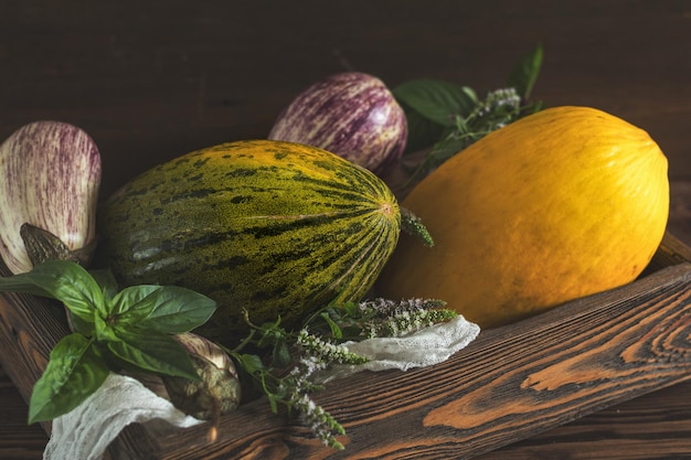 Melón albahaca menta púrpura graffiti berenjenas cebolla y albahaca fresca verde en una caja de madera en un fondo de madera vintage en estilo rústico foto tonificada de enfoque selectivo