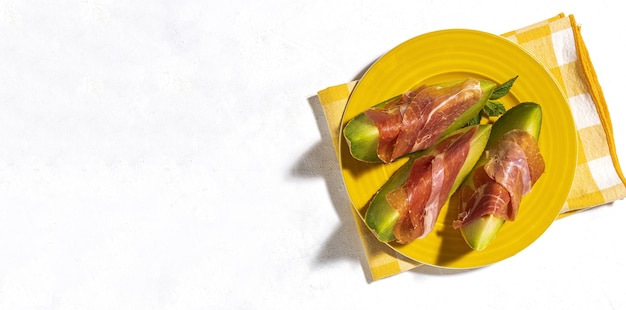 Melón fresco en rodajas con jamón con luz solar sobre fondos coloridos. Concepto de comida española