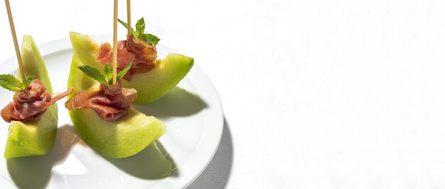 Melón fresco en rodajas con jamón con luz solar sobre fondos coloridos. Concepto de comida española