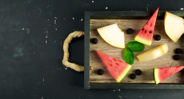 Melón, sandía, moras y menta en una bandeja de madera.