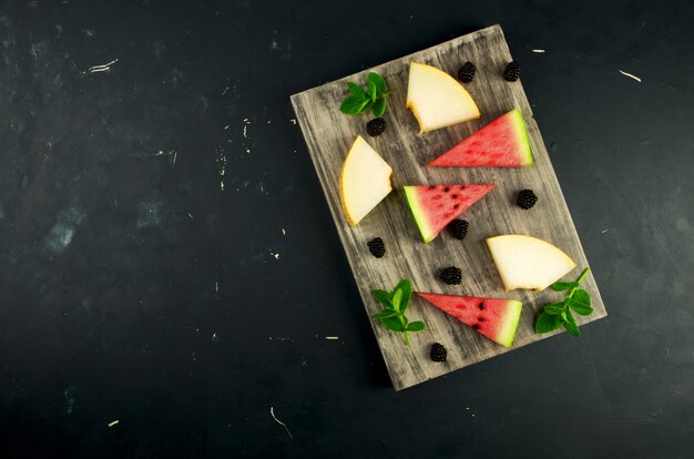 Melón, sandía, moras y menta en una mesa de madera