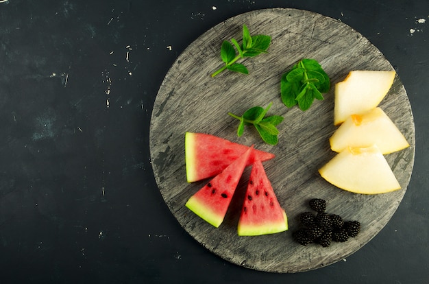 Melón, sandía, moras y menta en una mesa de madera