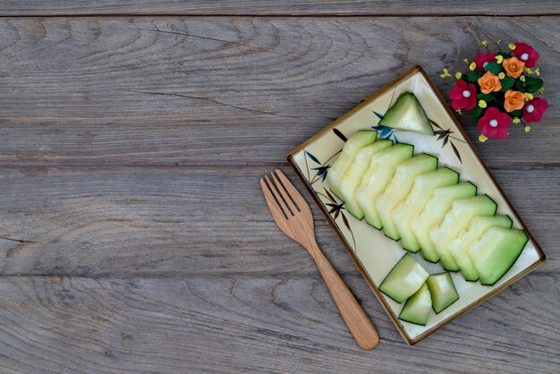 Melone in Scheiben auf einer Schüssel mit Holzvorke, Holztisch