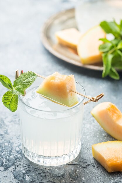 Melonenlimonade mit Eis und Minze in einem Glas auf dem Sommer-Erfrischungsgetränk des grauen Tisches