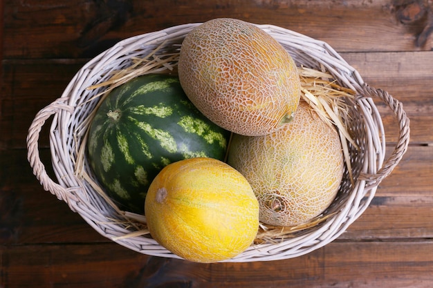 Melones y sandías en cesta de mimbre ovalada sobre fondo de madera