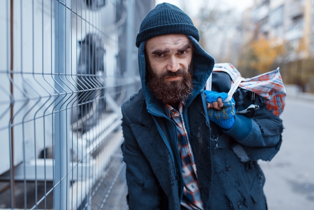 Mendigo barbudo masculino com bolsa na rua da cidade.