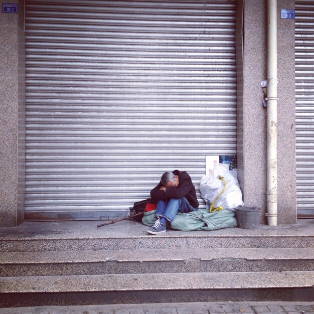 Mendigo sentado frente a una tienda cerrada