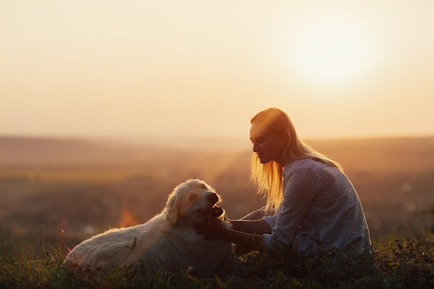 Menina abraça cachorro retriever na noite de verão ao pôr do sol