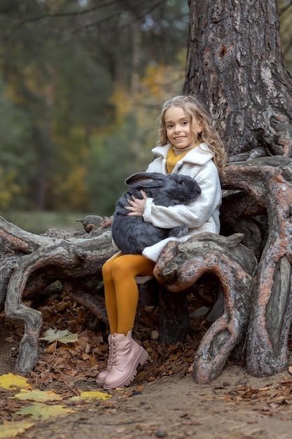 Menina abraça um coelho cinza gigante na floresta de outono Conceito amor pela natureza e amor pelos animais