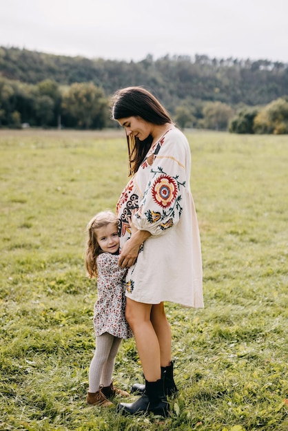 Foto menina abraçando a barriga de sua mãe grávida ouvindo o que está acontecendo dentro da barriga em um campo