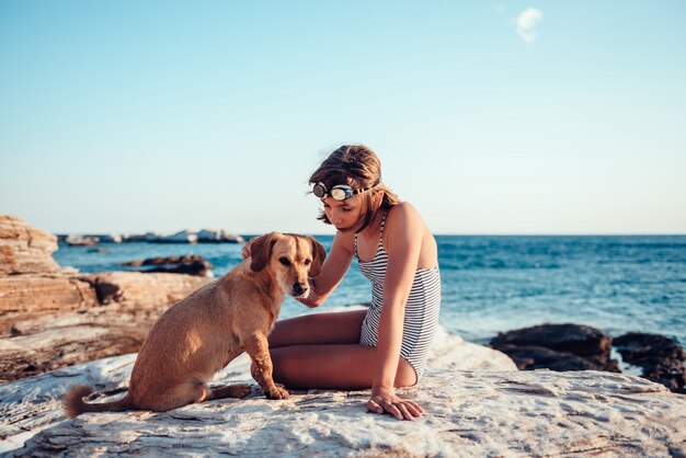 Menina abraçando seu cachorro enquanto está sentado na praia rochosa