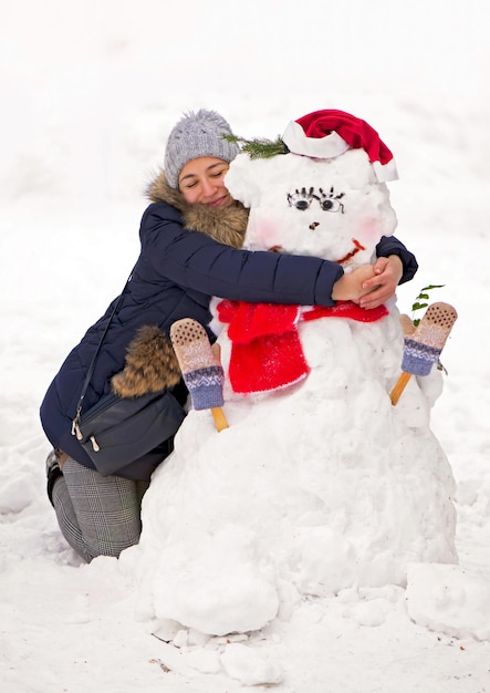 Menina abraçando um boneco de neve tema de inverno menina abraçando um boneco de neve ao ar livre