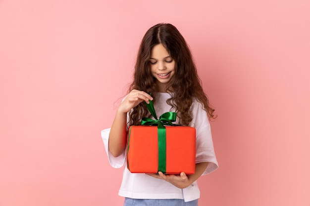 Foto menina abrindo a caixa de presentes desembrulhando o presente de aniversário para comemorar o feriado puxando a fita