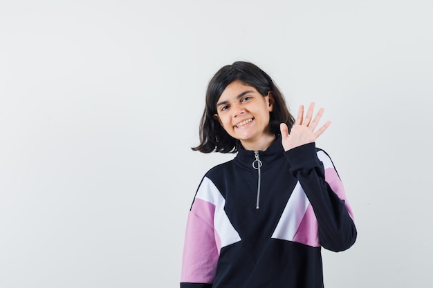 Menina acenando com a mão para saudação na camisa e parece feliz. vista frontal.