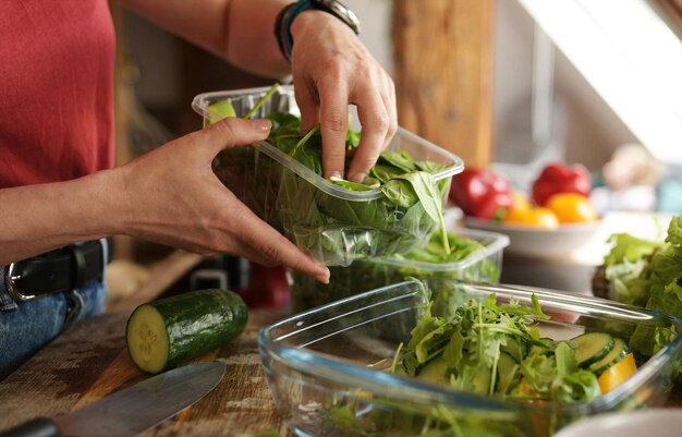 Menina adicionando verduras frescas e rúcula à salada de vegetais frescos na tigela na cozinha