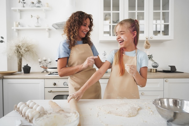 Menina adolescente ajudando a mãe a cozinhar massa na cozinha de casa