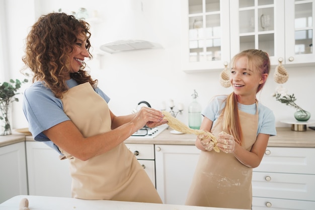 Menina adolescente ajudando a mãe a cozinhar massa na cozinha de casa