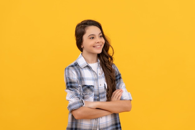 Menina adolescente alegre na camisa quadriculada e com cabelo longo encaracolado no fundo amarelo