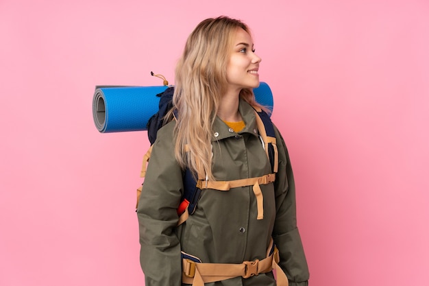 Menina adolescente alpinista com uma grande mochila isolada no lado rosa