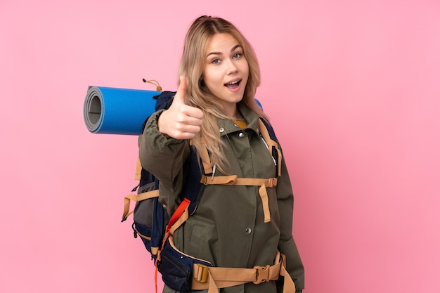 Menina adolescente alpinista com uma mochila grande e polegar para cima