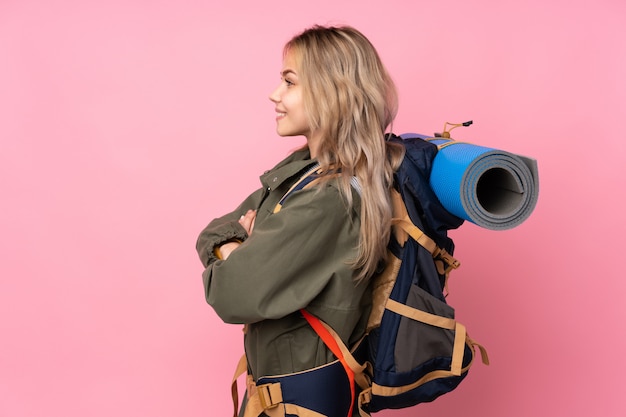 Menina adolescente alpinista com uma mochila grande na parede rosa em posição lateral