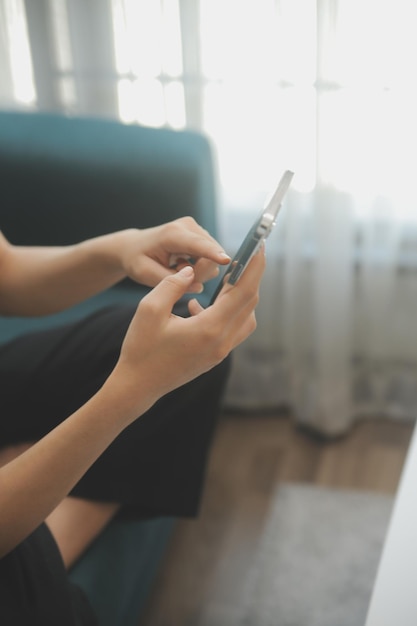 Menina adolescente asiática feliz segurando o dispositivo de computador pad usando tecnologia de tablet digital sentada no sofá em casa Jovem sorridente usando aplicativos de compras on-line lendo notícias navegando na internet no sofá