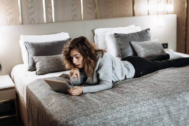 Menina adolescente assistindo vídeo no tablet deitado na cama