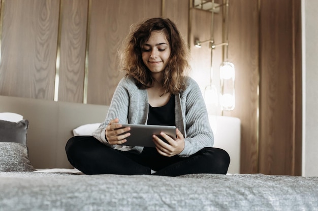 Menina adolescente assistindo vídeo ou lendo livro no tablet na cama