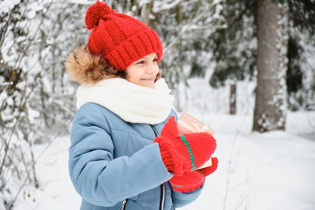 Menina adolescente bonita abre uma caixa de presente presente de natal ao ar livre no inverno criança em luvas de cachecol e chapéu
