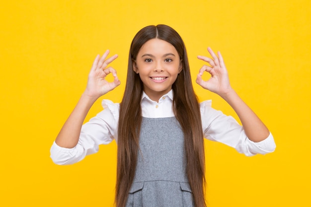 Menina adolescente bonitinha fazendo gesto de Ok em fundo amarelo Garota feliz enfrenta emoções positivas e sorridentes