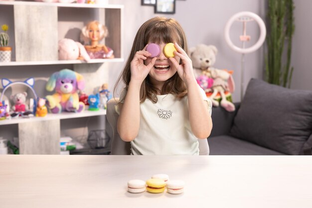 Menina adolescente brinca com macarons de sobremesa segurando os biscoitos como óculos ao redor dos olhos