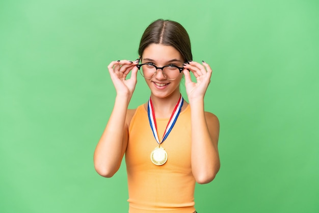 Menina adolescente caucasiana com medalhas sobre fundo isolado com óculos e surpresa