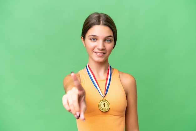 Menina adolescente caucasiana com medalhas sobre fundo isolado mostrando e levantando um dedo