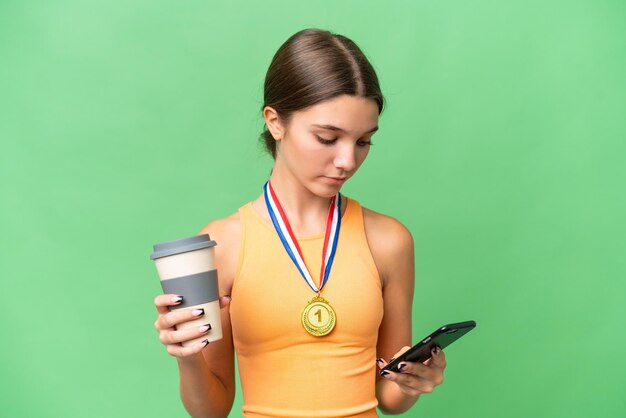 Menina adolescente caucasiana com medalhas sobre fundo isolado segurando café para levar e um celular