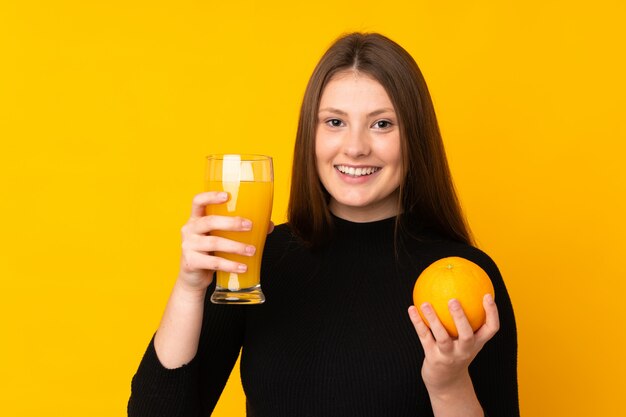 Menina adolescente caucasiano segurando uma laranja sobre amarelo isolado