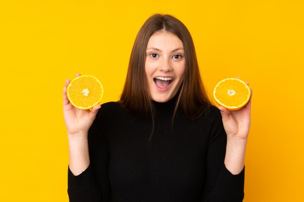 Menina adolescente caucasiano segurando uma laranja sobre amarelo isolado