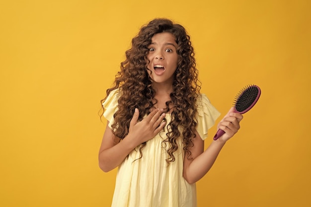 Menina adolescente chocada com cabelo longo encaracolado segurando escova de pente para pentear hábitos diários