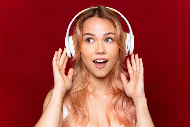 Menina adolescente com cabelo rosa ouvindo música no vermelho isolado