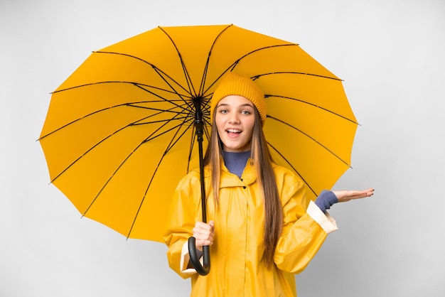 Menina adolescente com casaco à prova de chuva e guarda-chuva sobre fundo branco isolado com expressão facial chocada